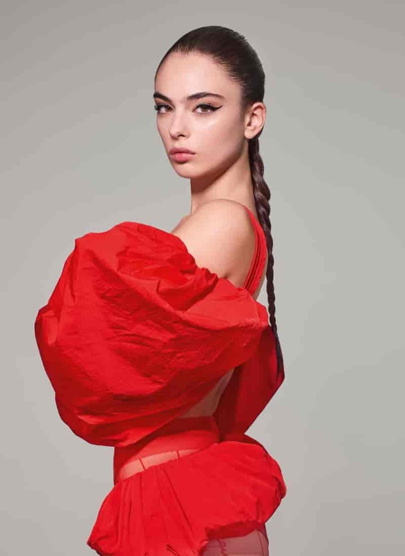 Actress and model Deva Cassel strikes a bold pose in a voluminous red ensemble from Jacquemus, her hair styled in a sleek braid.
